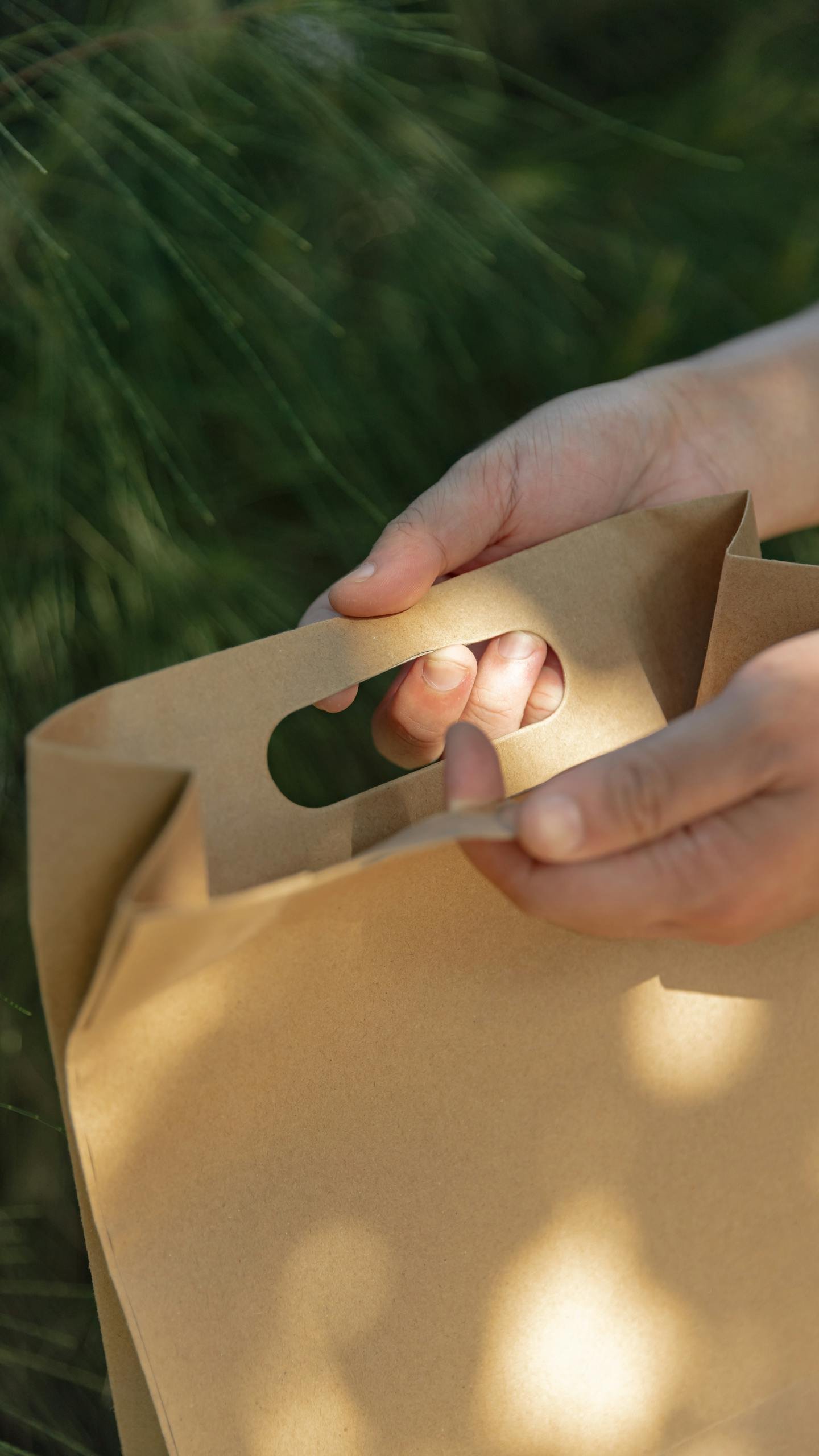 Close-up of a hand holding an eco-friendly paper bag outdoors in sunlight.